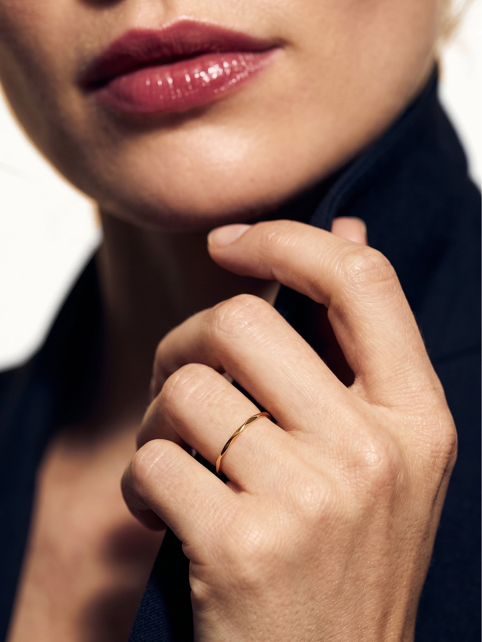 Whisper Band – worn on a hand raised to the collar, close-up, gold, dark blazer, ivory studio background