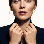 Whisper Band – worn with both hands holding the blazer collar, gold, dark blazer, ivory studio background