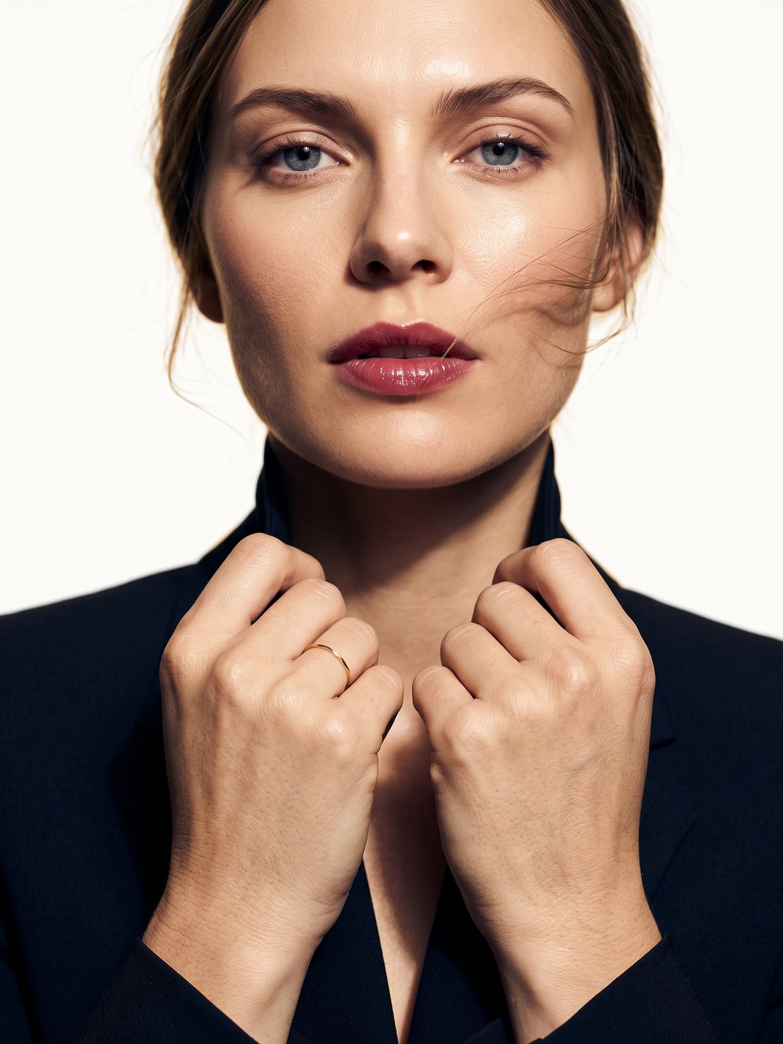 Whisper Band – worn with both hands holding the blazer collar, gold, dark blazer, ivory studio background
