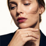 Whisper Band – worn on a hand resting beneath the chin, gold, dark blazer, ivory studio background