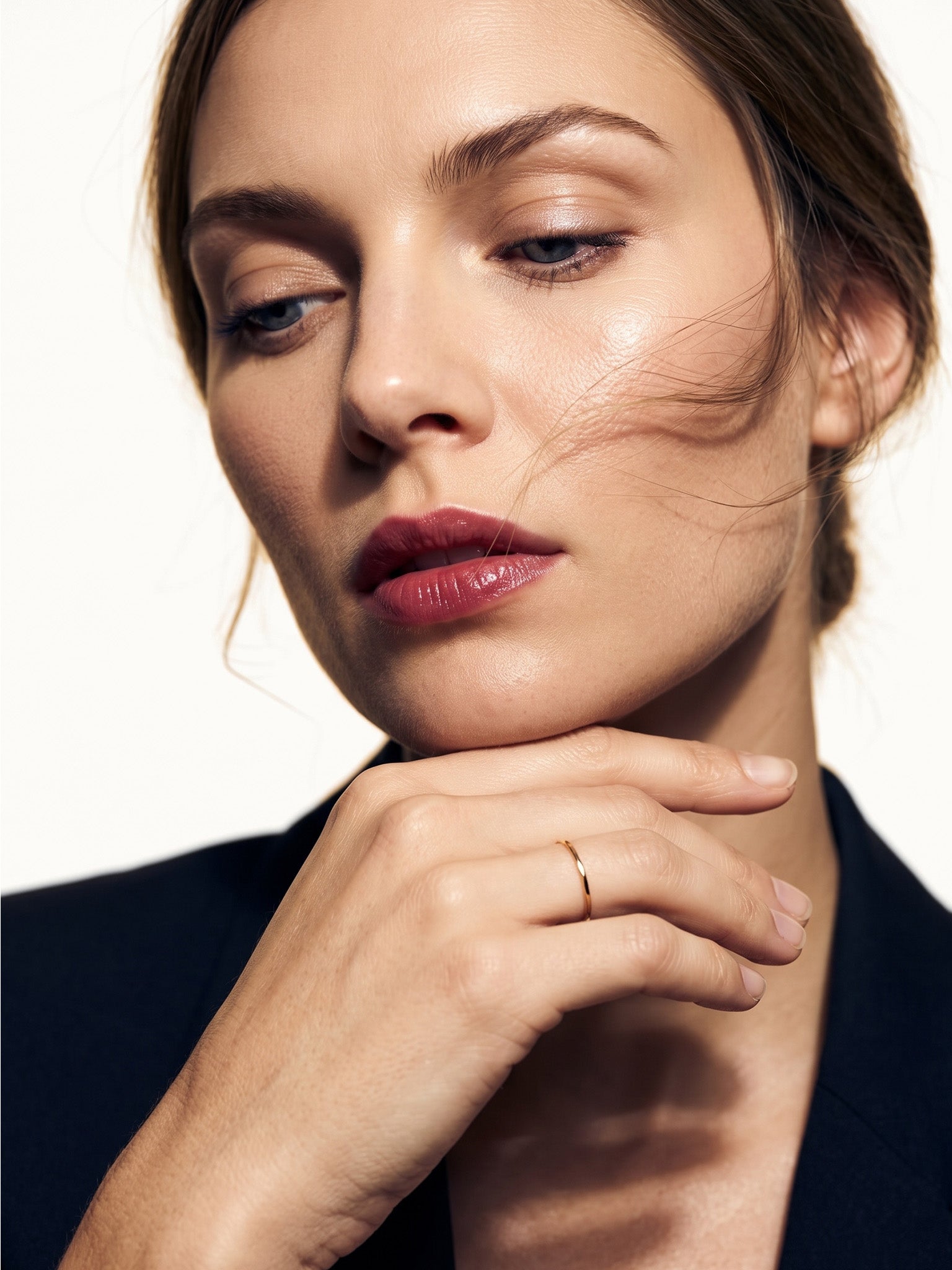 Whisper Band – worn on a hand resting beneath the chin, gold, dark blazer, ivory studio background