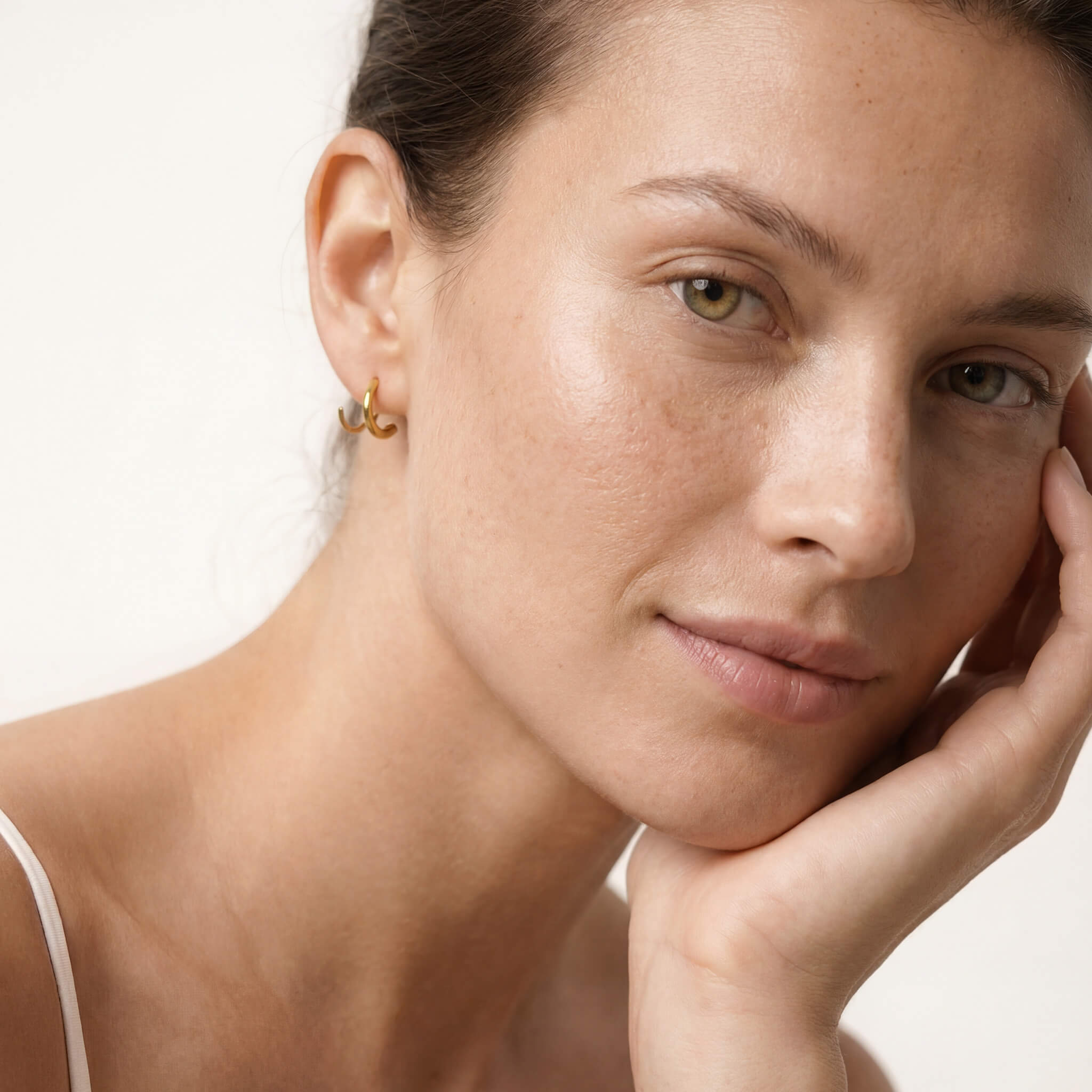 Whisper Hoops – worn in the ear, hand resting at the cheek, gold, bare shoulders