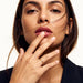 Woven Eternity Ring – worn with fingertips raised to the lips, gold, dark blazer, ivory studio background